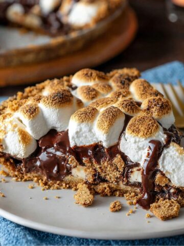 s'mores pie slice with toasted marshmallows, melted chocolate, and graham cracker crust on a plate with a gold fork.