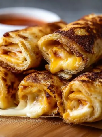 Easy Homemade Grilled Cheese Roll Ups with melted cheese inside, stacked on a wooden board and served with tomato soup.