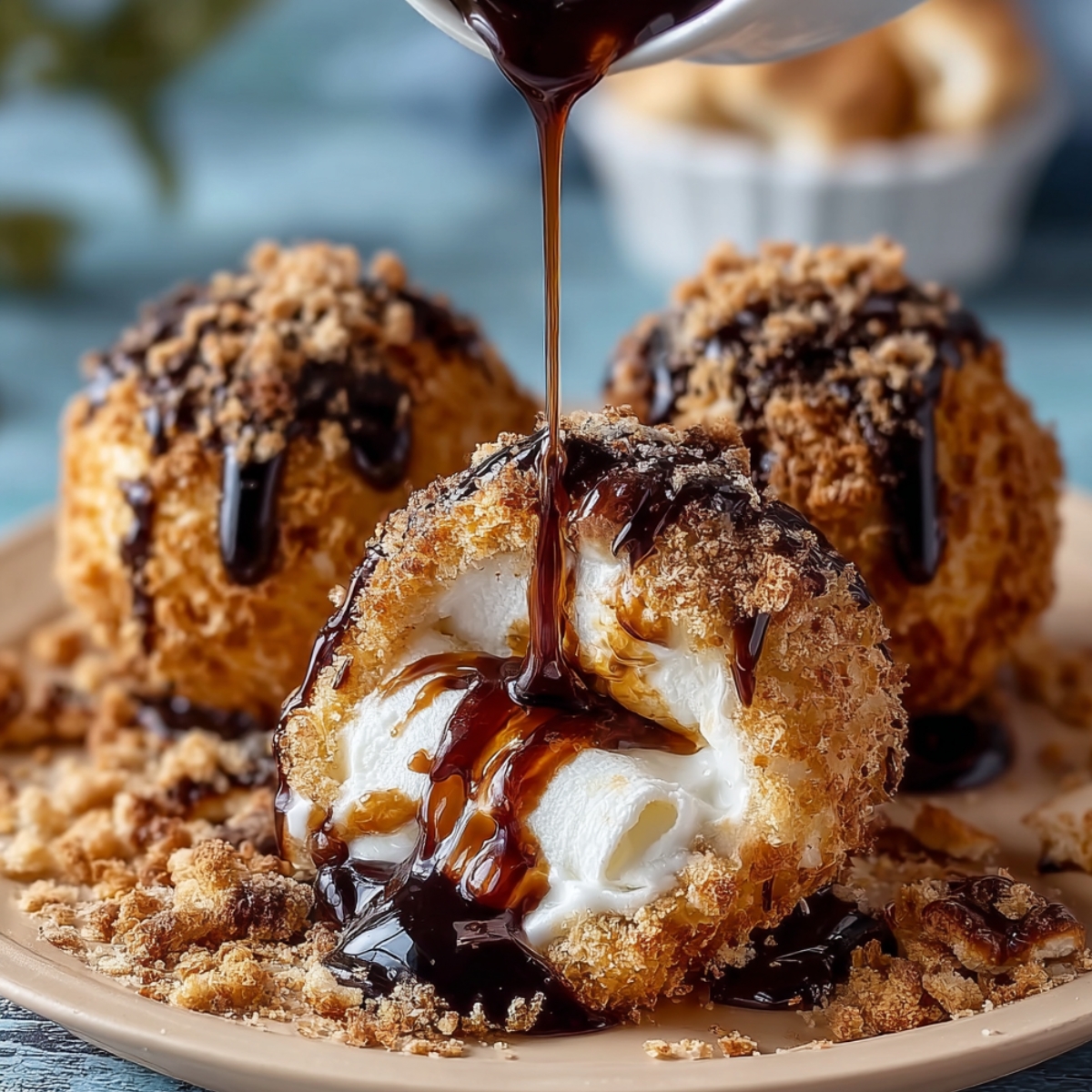 Homemade fried s’mores bombs on a white plate, two split open with gooey marshmallow and caramel oozing out, topped with chocolate drizzle and graham crumbs.