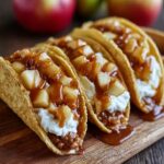 Homemade apple cheesecake tacos with cinnamon sugar shells, whipped cheesecake filling, diced apples, and caramel drizzle on a wooden board.