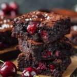 Homemade Chocolate Cherry Brownies with glossy red cherries in a fudgy interior, crinkled crust sprinkled with sea salt, and fresh cherries nearby.
