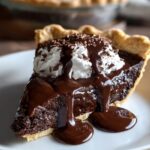 Homemade Hot Fudge Pie with whipped cream, chocolate sauce, and shavings on a white plate.