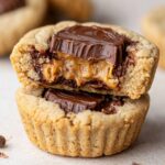 Homemade Peanut Butter Cup Cookies with a bite taken out, showing a gooey peanut butter center and melted chocolate, stacked on another soft, golden cookie.