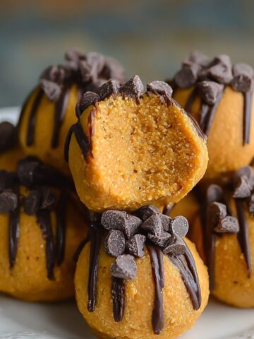 Homemade pumpkin cheesecake truffles coated in graham cracker crumbs, topped with mini chocolate chips, and one cut open to reveal smooth pumpkin cheesecake filling on a rustic plate.