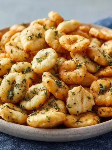 Homemade ranch oyster crackers in a shallow ceramic bowl, golden brown and coated with herbs.