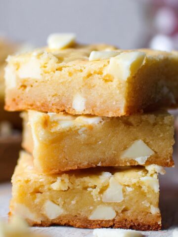 Homemade White Chocolate Brownies with chunks inside, on a rustic wooden surface.