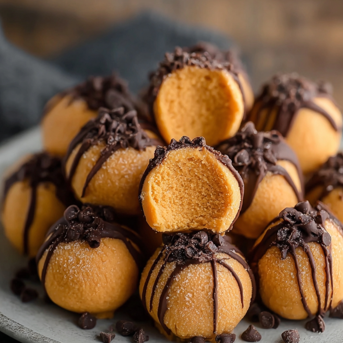 Homemade pumpkin cheesecake truffles drizzled with dark chocolate, topped with chocolate chips, and one cut open to reveal smooth pumpkin filling on a white plate.