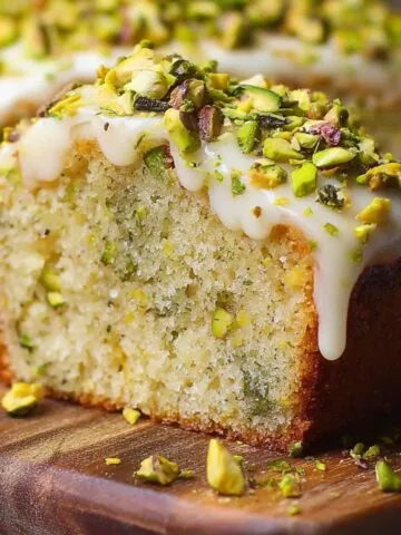 Moist Lemon Pistachio Cake slice with lemon glaze and chopped pistachios on top, moist crumb inside, sitting on a wooden board.