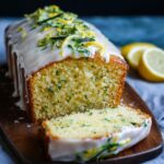 Moist homemade lemon zucchini cake with white lemon glaze and fresh zucchini-lemon zest topping, sliced on a wooden board