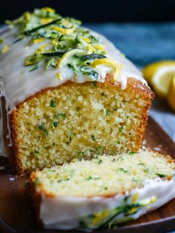 Moist homemade lemon zucchini cake with white lemon glaze and fresh zucchini-lemon zest topping, sliced on a wooden board