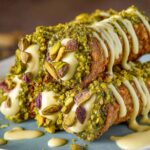 Close-up of homemade pistachio cannoli with creamy filling, chopped pistachios, and drizzle.