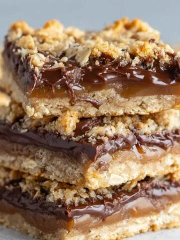 The Best Oatmeal Fudge Bars stacked on parchment, showing a golden oat base, thick chocolate layer, and crumbly oat topping.