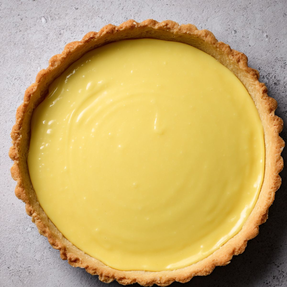 Homemade Mango Key Lime Pie with a golden, crimped crust and smooth, glossy yellow filling, set on a light grey surface.