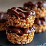 Two stacked homemade Chocolate Peanut Butter Rice Krispie Cups with a crispy peanut butter base and glossy chocolate topping, on a rustic surface.