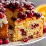 Homemade cranberry orange cake slice topped with cranberries, glaze, and powdered sugar.