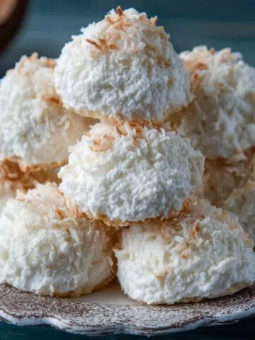 Homemade coconut meringue cookies stacked on a vintage patterned plate, with golden toasted coconut edges and a rustic homemade look.