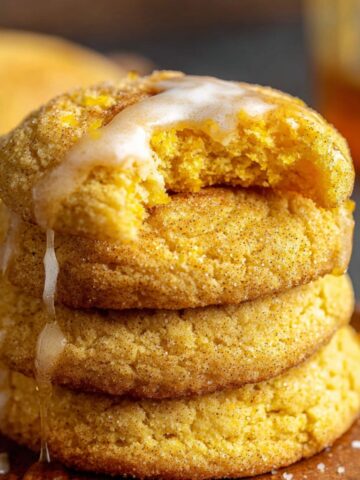 Homemade Cornbread Cookies Recipe with cinnamon sugar, one bitten to reveal a soft interior, topped with a cinnamon glaze. Warm, rustic background.
