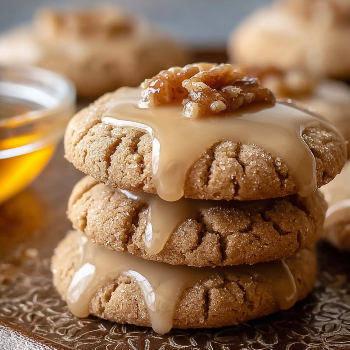 Homemade Maple Cookies Recipe topped with glossy maple glaze and chopped nuts, with glaze dripping down the top cookie, on a rustic tray with scattered nut pieces.