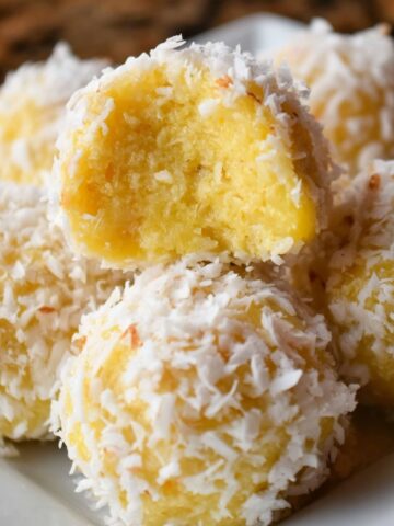 Homemade pineapple coconut balls on a white plate, one with a bite showing the soft yellow center.