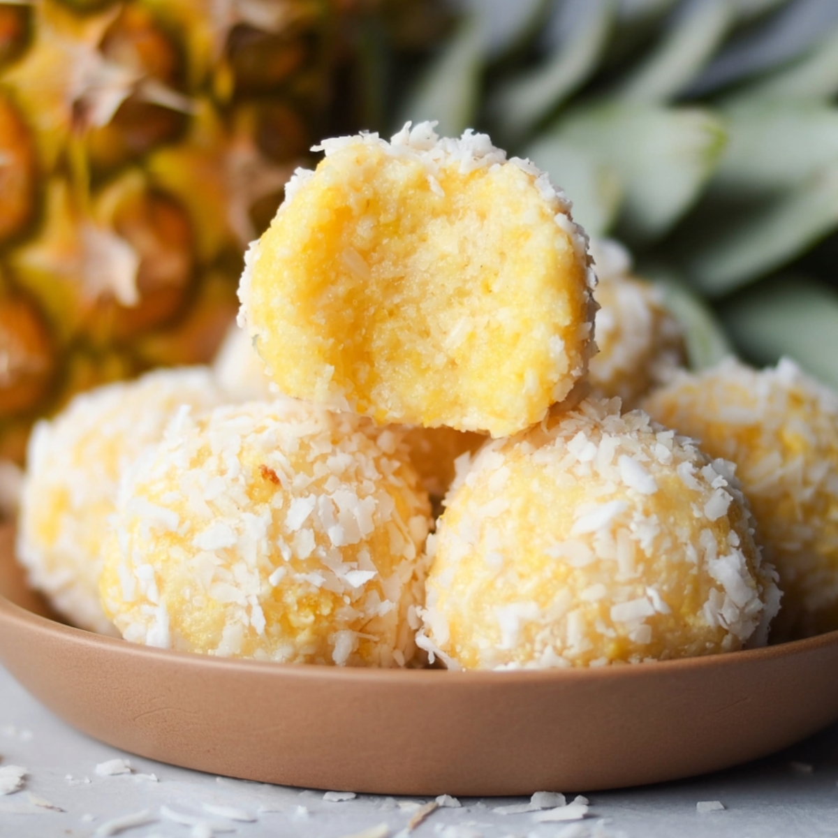 Homemade pineapple coconut balls in a bowl, one with a bite showing the soft yellow center.