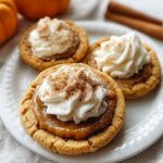 Pumpkin Pie Cookie Recipe on a white plate, topped with swirls of frosting and cinnamon, with pumpkins and cinnamon sticks in the background.