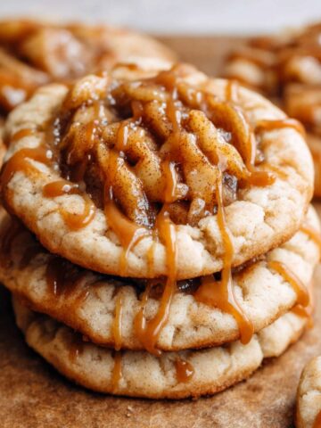 Apple Pie Cookies drizzled with golden caramel sauce, topped with warm cinnamon-spiced apple filling, sitting on a rustic wooden surface.