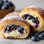 Blueberry Cream Cheese Crescent Rolls with golden flaky pastry, creamy filling, and juicy blueberries, dusted with powdered sugar on a light surface.