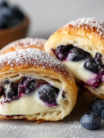 Blueberry Cream Cheese Crescent Rolls with golden flaky pastry, creamy filling, and juicy blueberries, dusted with powdered sugar on a light surface.