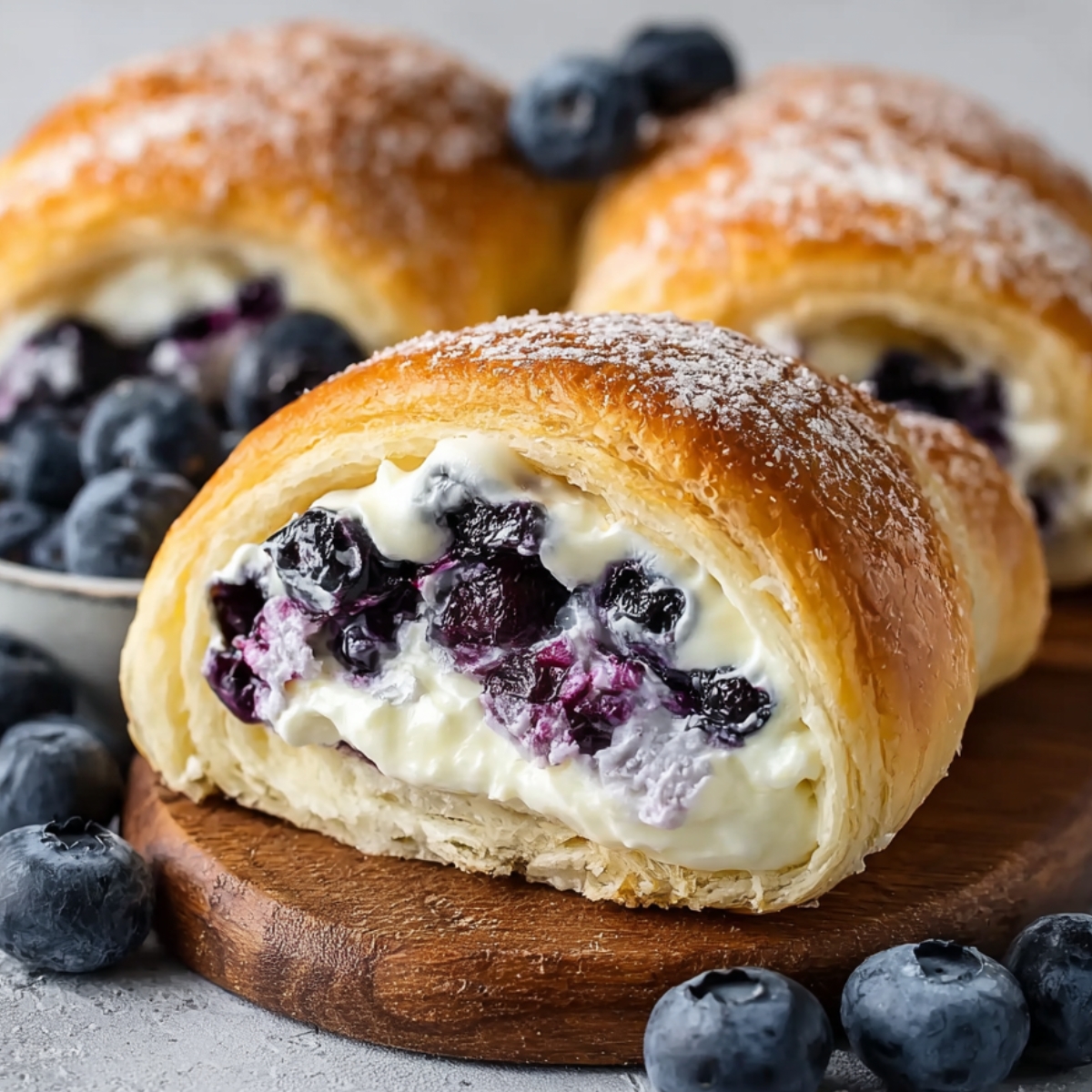 Easy Blueberry Cream Cheese Crescent Rolls filled with creamy cheese and juicy blueberries, dusted with powdered sugar on a light surface.