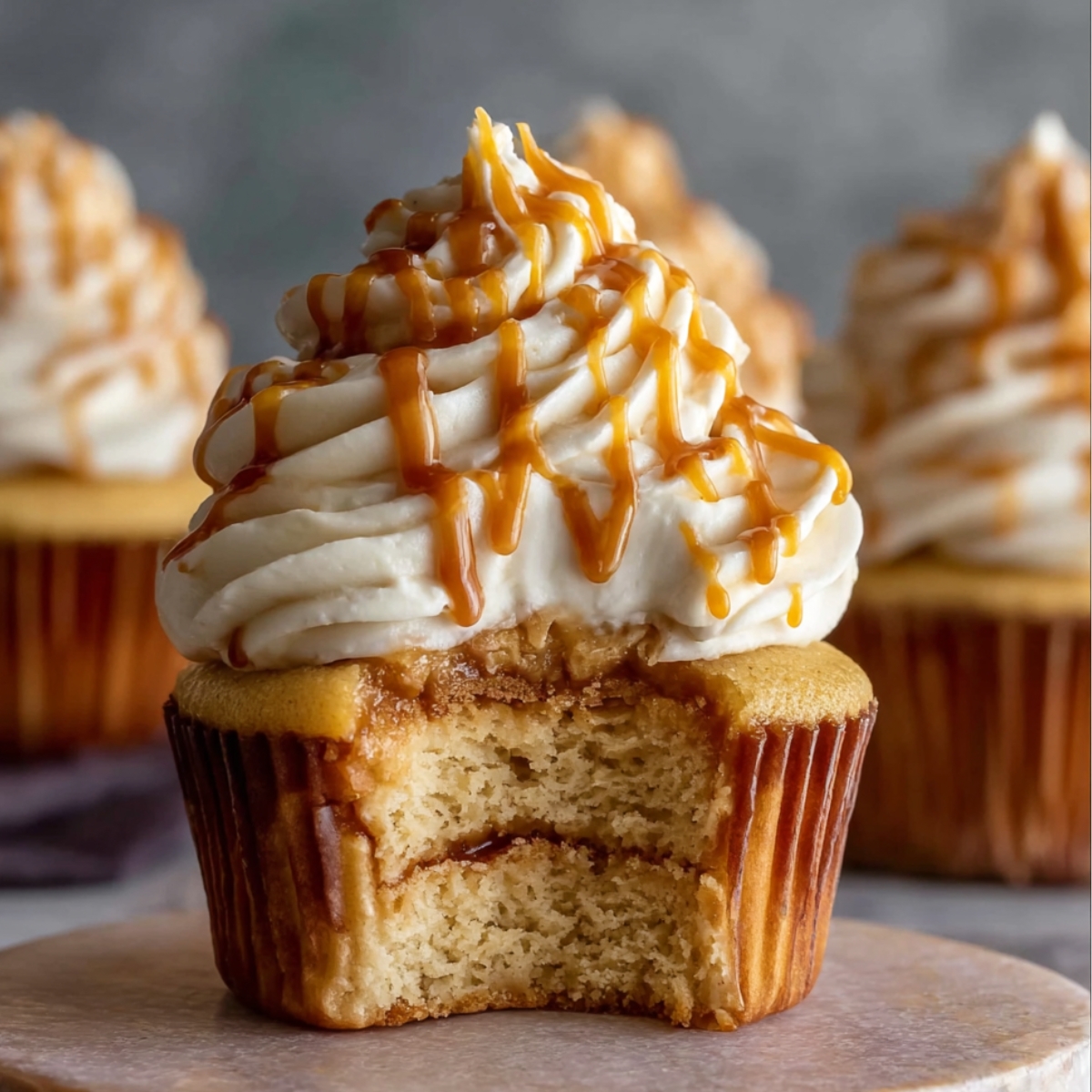 Easy Harry Potter Butterbeer Cupcakes with creamy butterscotch filling, topped with whipped frosting and caramel drizzle, cupcake liner peeled back to show the soft vanilla cake and gooey center.