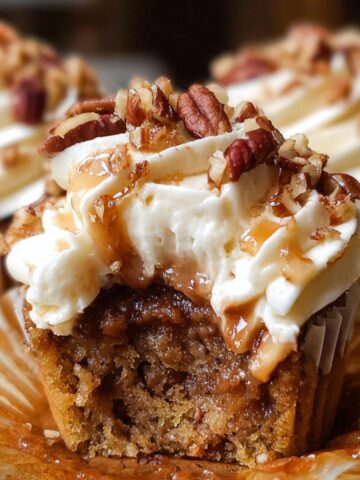Close-up of a homemade pecan pie cupcakes with creamy frosting, caramel drizzle, and chopped pecans on top, showing a gooey brown pecan filling inside a moist golden cupcake.
