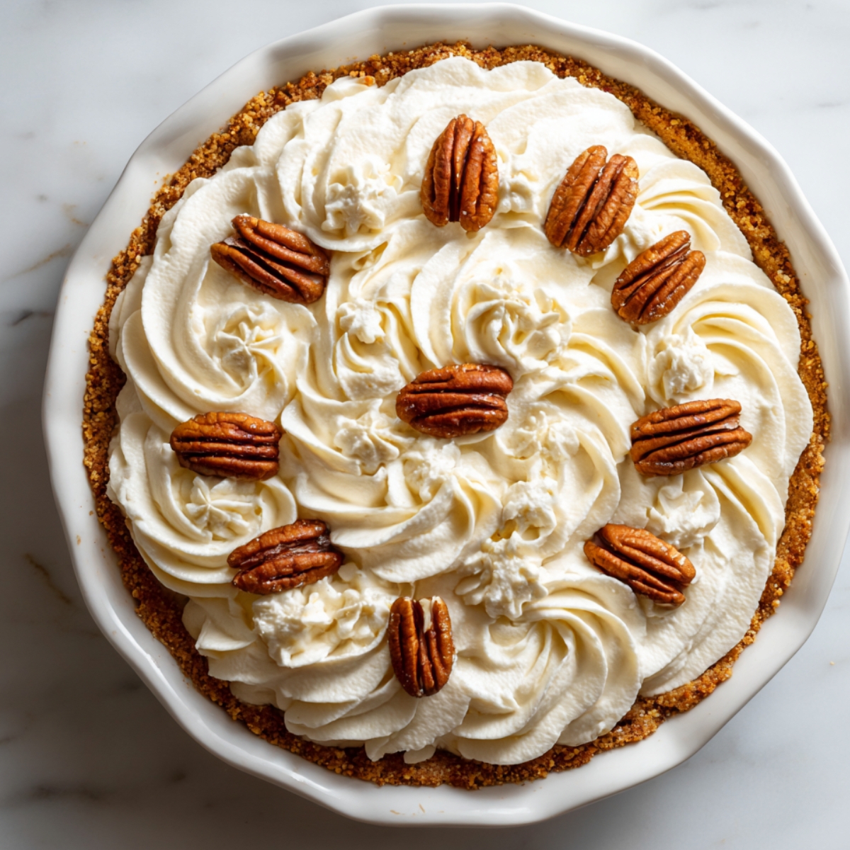 Homemade Southern possum pie with a golden pecan crust, topped with swirls of whipped cream and whole pecans in a white ceramic dish on a marble countertop.