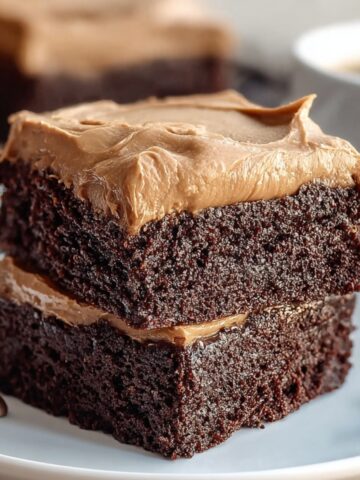 Frosted Coffee Brownies stacked on a white plate, topped with creamy coffee frosting and surrounded by coffee beans.