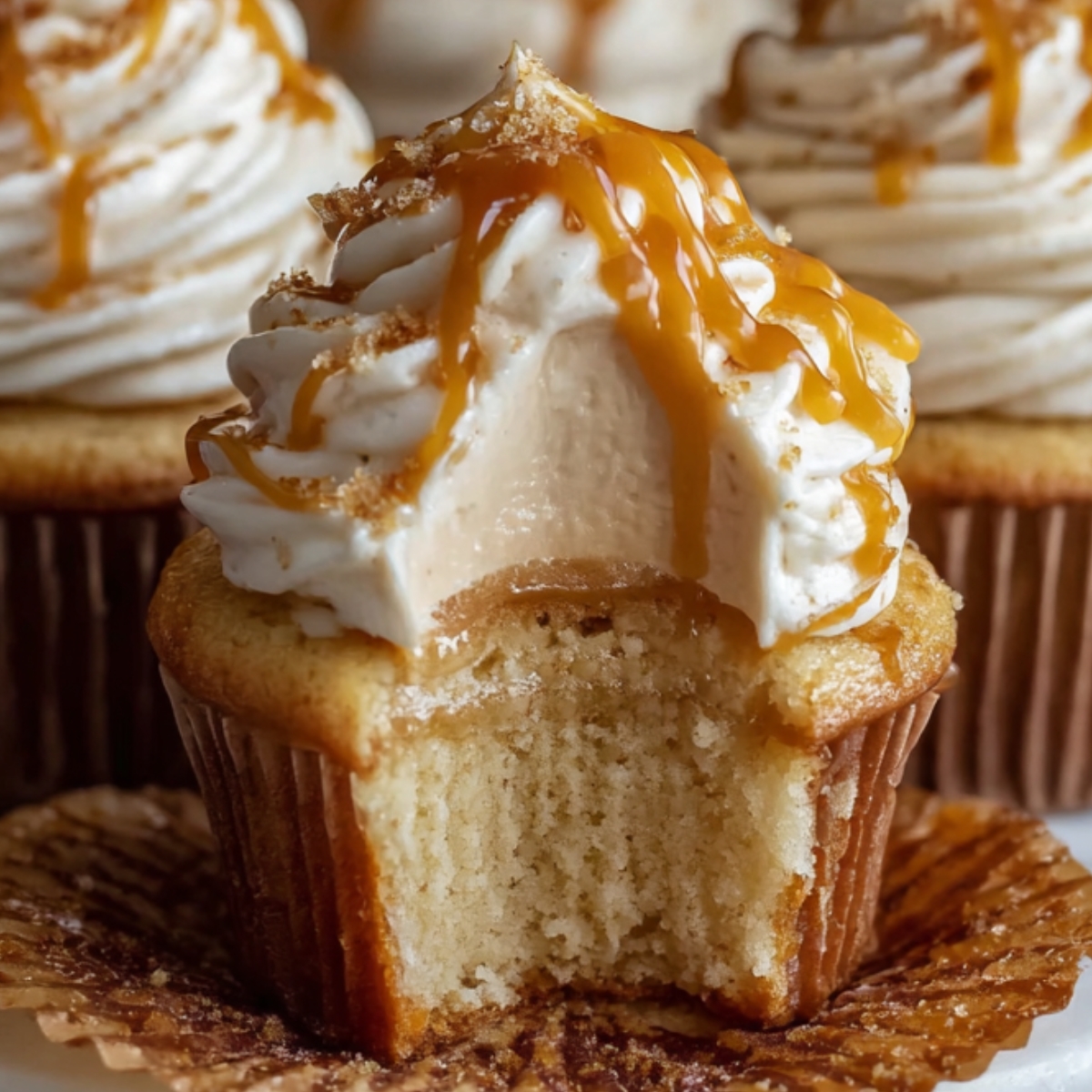 Homemade Harry Potter Butterbeer cupcakes with fluffy butterscotch frosting and caramel drizzle, showing a soft golden crumb with a bite taken out to reveal a gooey caramel center.