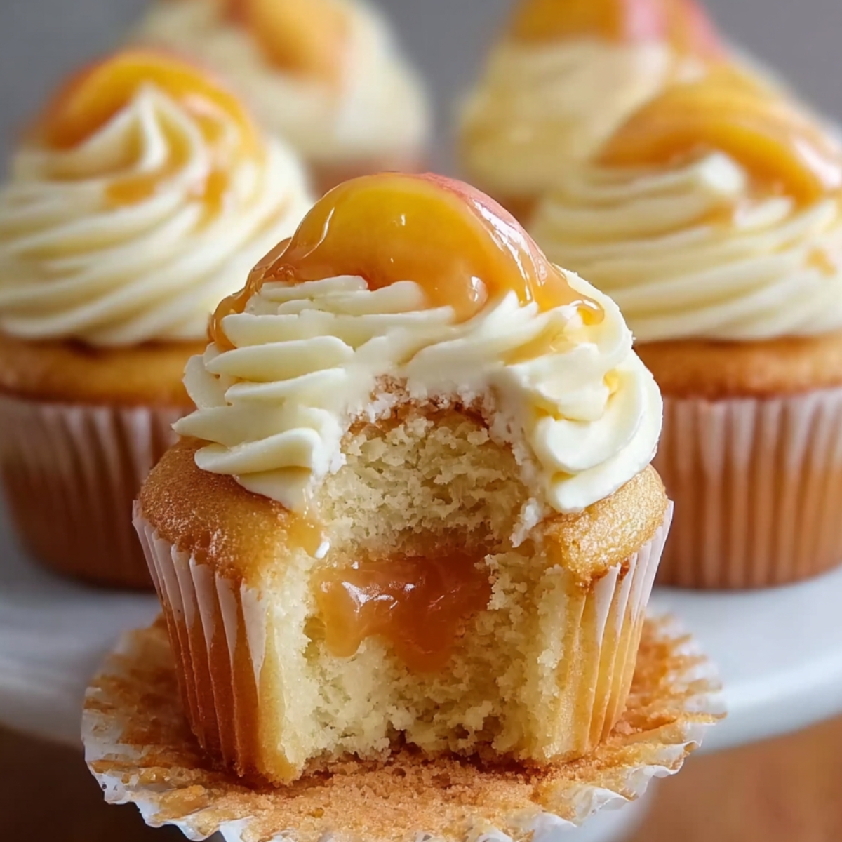 Healthy Honey Peach Cream Cheese Cupcakes with a bite taken out, showing peach filling, topped with cream cheese frosting, a peach slice, and a honey drizzle.