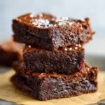 Homemade Chickpea Brownies on parchment paper with melted chocolate oozing between layers, homemade and gooey.
