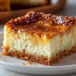 Homemade Neiman Marcus Cake slice on a white plate with crumbs, showing creamy layers and warm homemade lighting.