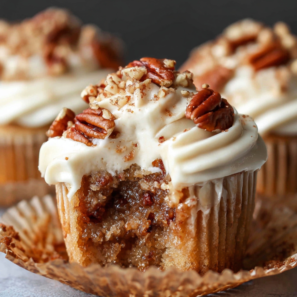 Homemade Pecan Pie Cupcakes with creamy frosting and chopped pecans, showing gooey pecan filling inside a golden cake on a wooden plate.