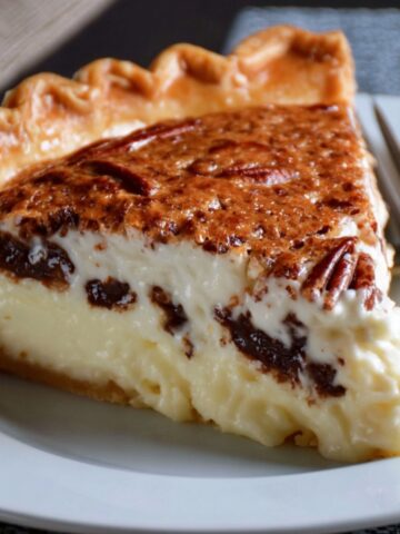 Homemade Possum Pie slice on a white plate, showing creamy vanilla and chocolate layers under a golden pecan crust with a fork beside it in soft natural light.