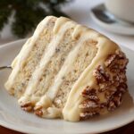 Homemade Snowy Bavarian Bliss Cake slice with soft vanilla layers, creamy white frosting, and pecans on a white plate, captured in warm natural light.