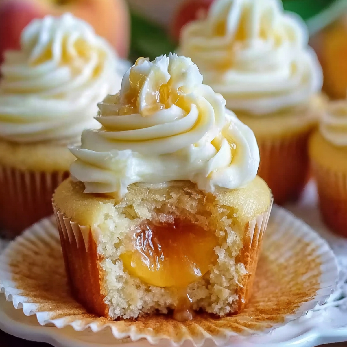 A close-up of a homemade honey peach cream cheese cupcakes with a bite taken out, showing peach filling, topped with cream cheese frosting, a peach slice, and a honey drizzle.
