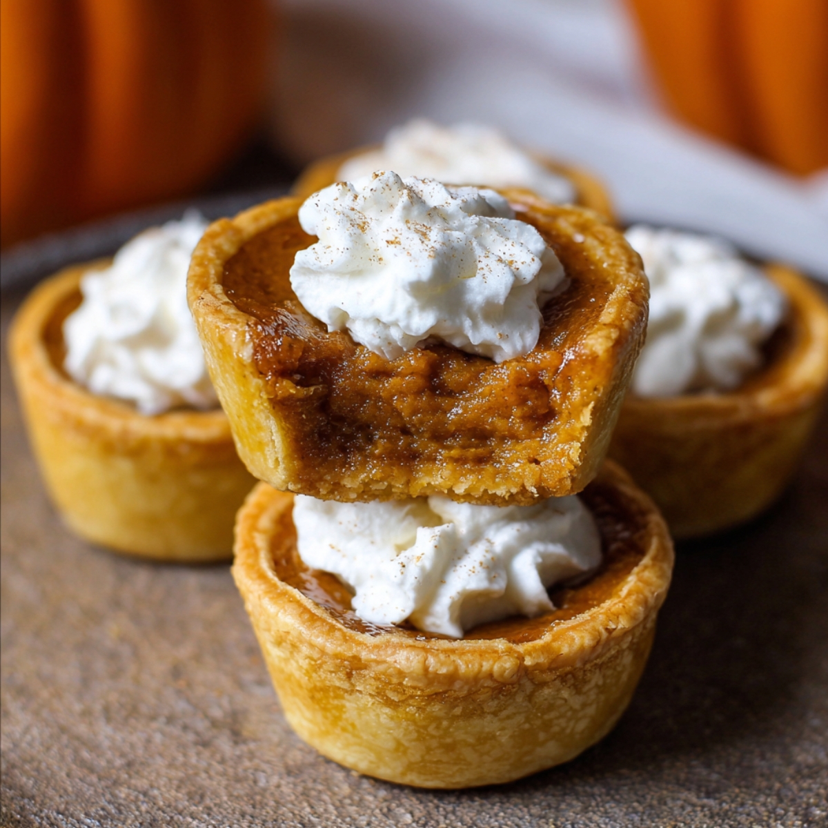 Homemade mini pumpkin pies with flaky golden crusts, creamy pumpkin filling, and whipped cream on top, one with a bite taken out.