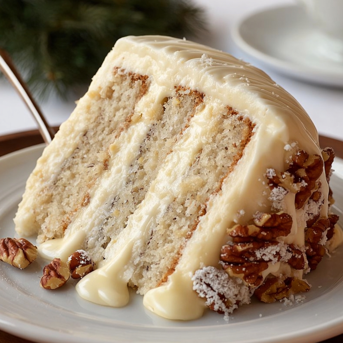 Close-up of a homemade Snowy Bavarian Bliss Cake slice with creamy white frosting and sugared pecans on a white plate in warm natural light.