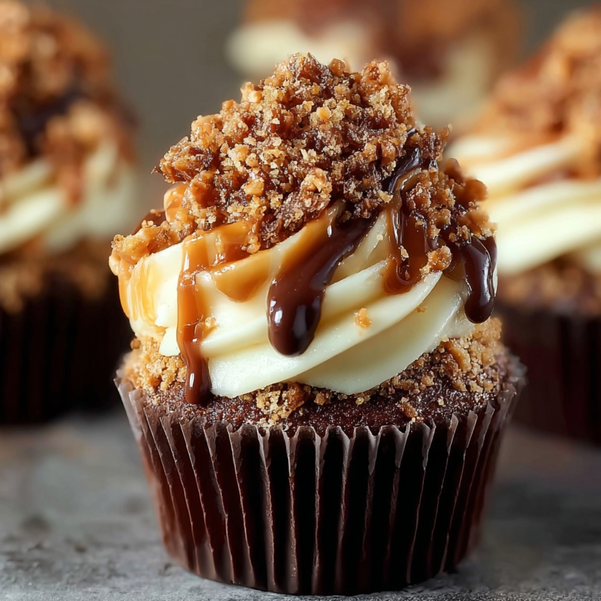 Close-up of homemade chocolate Toffee Crunch Cupcakes topped with vanilla frosting, caramel and chocolate drizzle, and crunchy toffee bits in warm natural light.