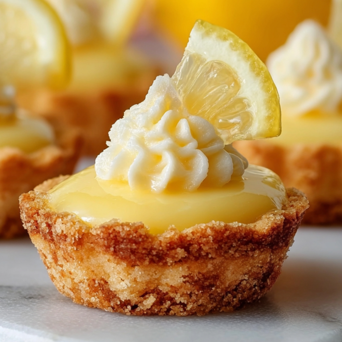 Lemon Curd Cookie Cups topped with whipped cream and a slice of fresh lemon on a marble surface.