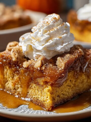 Pumpkin Spice Gooey Cake topped with whipped cream and cinnamon, with a gooey caramel layer and moist pumpkin base on a patterned plate.