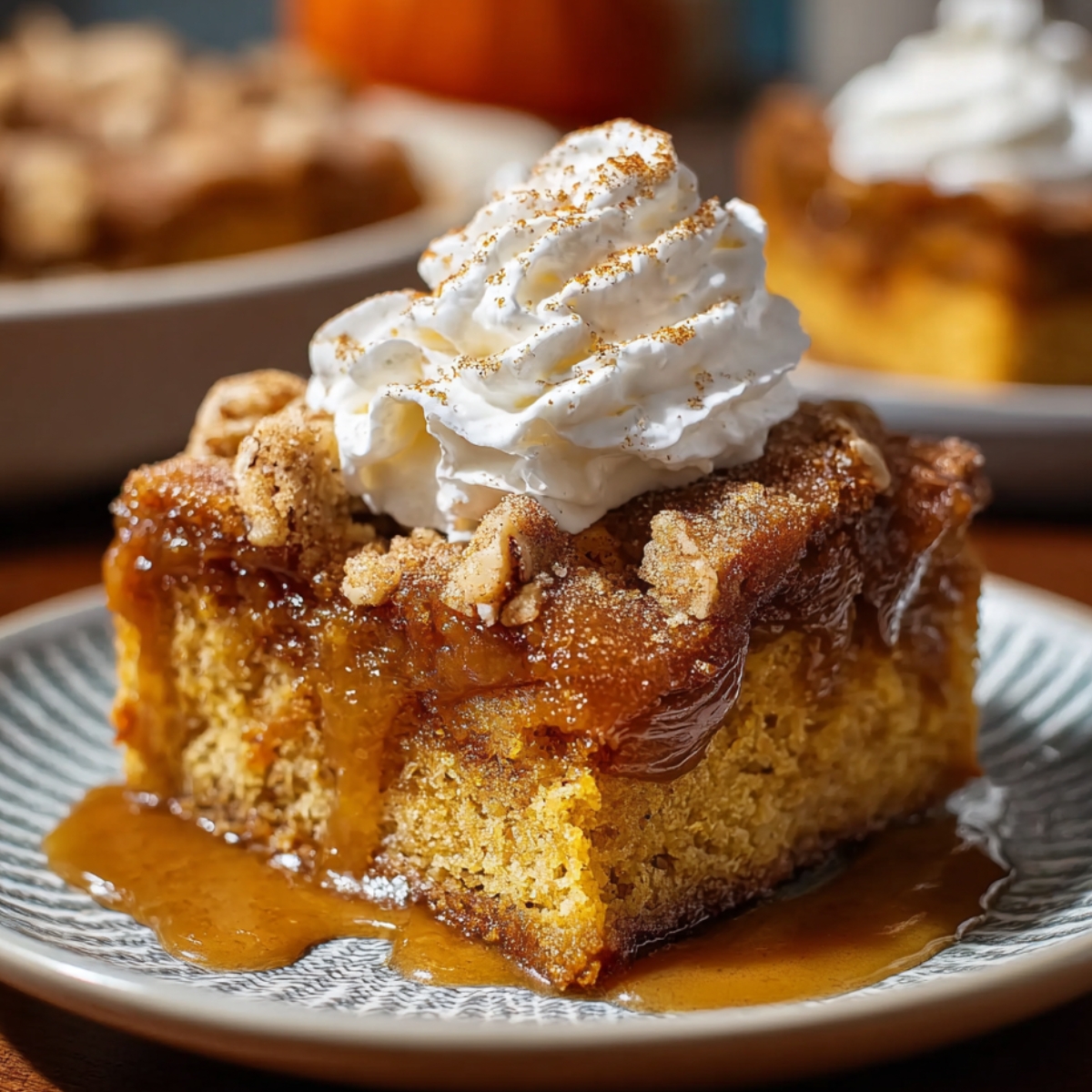 Pumpkin Spice Gooey Cake topped with whipped cream and cinnamon, with a gooey caramel layer and moist pumpkin base on a patterned plate.
