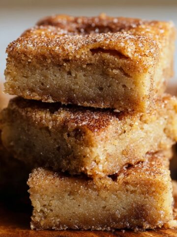 Best Cinnamon Sugar Blondies Recipe stacked on a wooden board, showing their moist, buttery texture and cinnamon sugar topping.