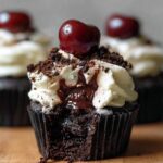 Black Forest Cupcakes with whipped cream, chocolate shavings, and a cherry on top, showing rich cherry filling oozing from the moist chocolate cake.