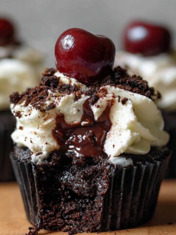 Black Forest Cupcakes with whipped cream, chocolate shavings, and a cherry on top, showing rich cherry filling oozing from the moist chocolate cake.